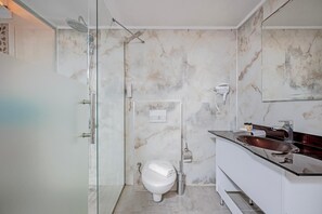 A modern bathroom with a glass shower enclosure, a white toilet, and a vanity with a dark countertop. - Dedeman Kemer Resort (Kemer)