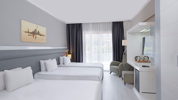 A modern hotel room with two beds, a desk, a chair, a TV, and a painting on the wall. - Dedeman Kemer Resort (Kemer)