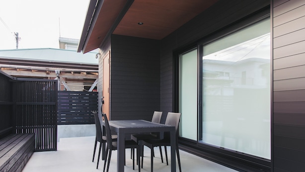 Un patio moderno al aire libre con mesa y sillas, un cerco de madera y un ventanal grande.