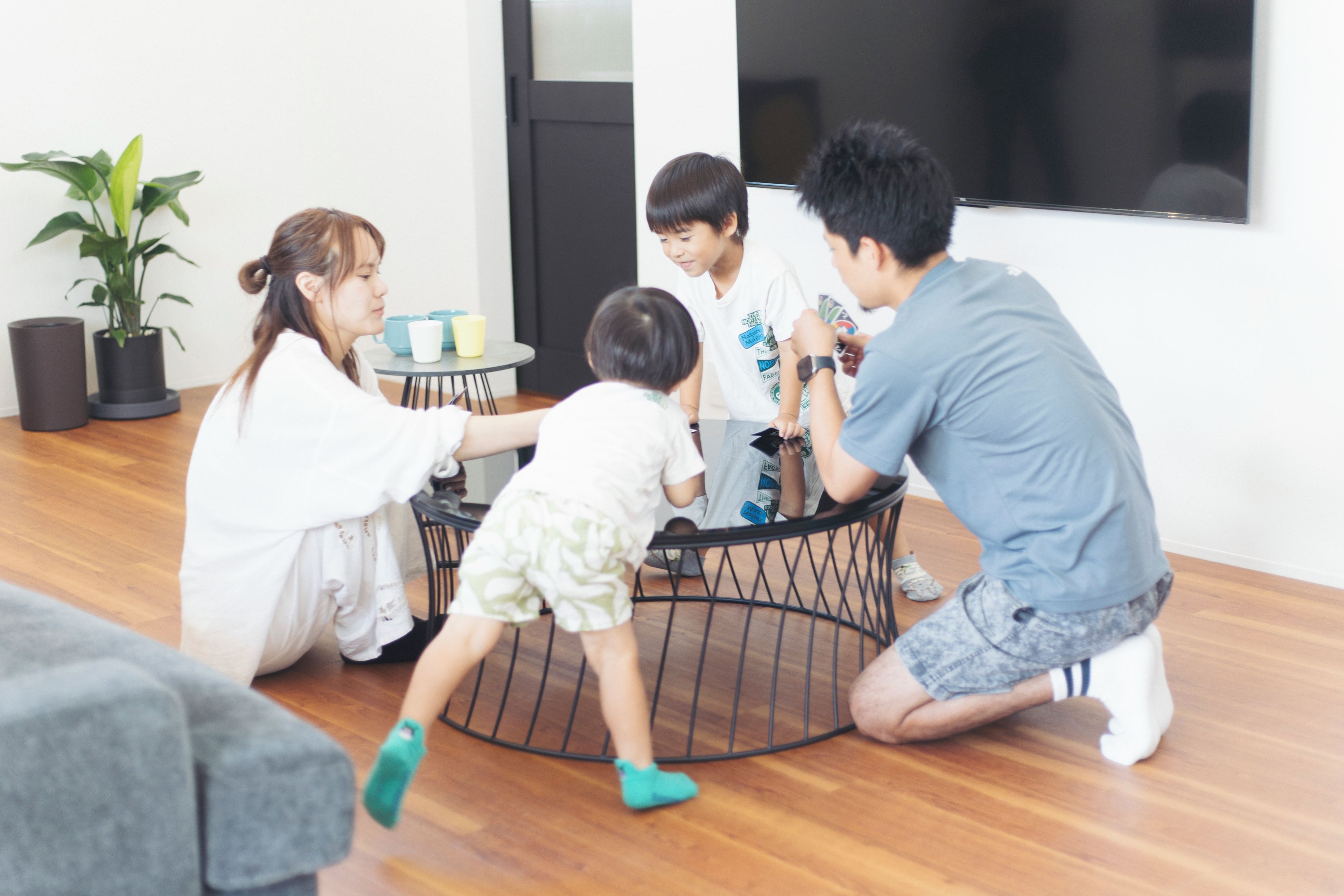 Eine Familie interagiert in einem modernen Wohnzimmer mit einem runden schwarzen Couchtisch, einem Blumentopf und einem großen Fenster.