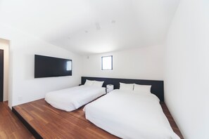 Une chambre d’hôtel moderne avec un grand lit, un téléviseur fixé au mur et une petite fenêtre.