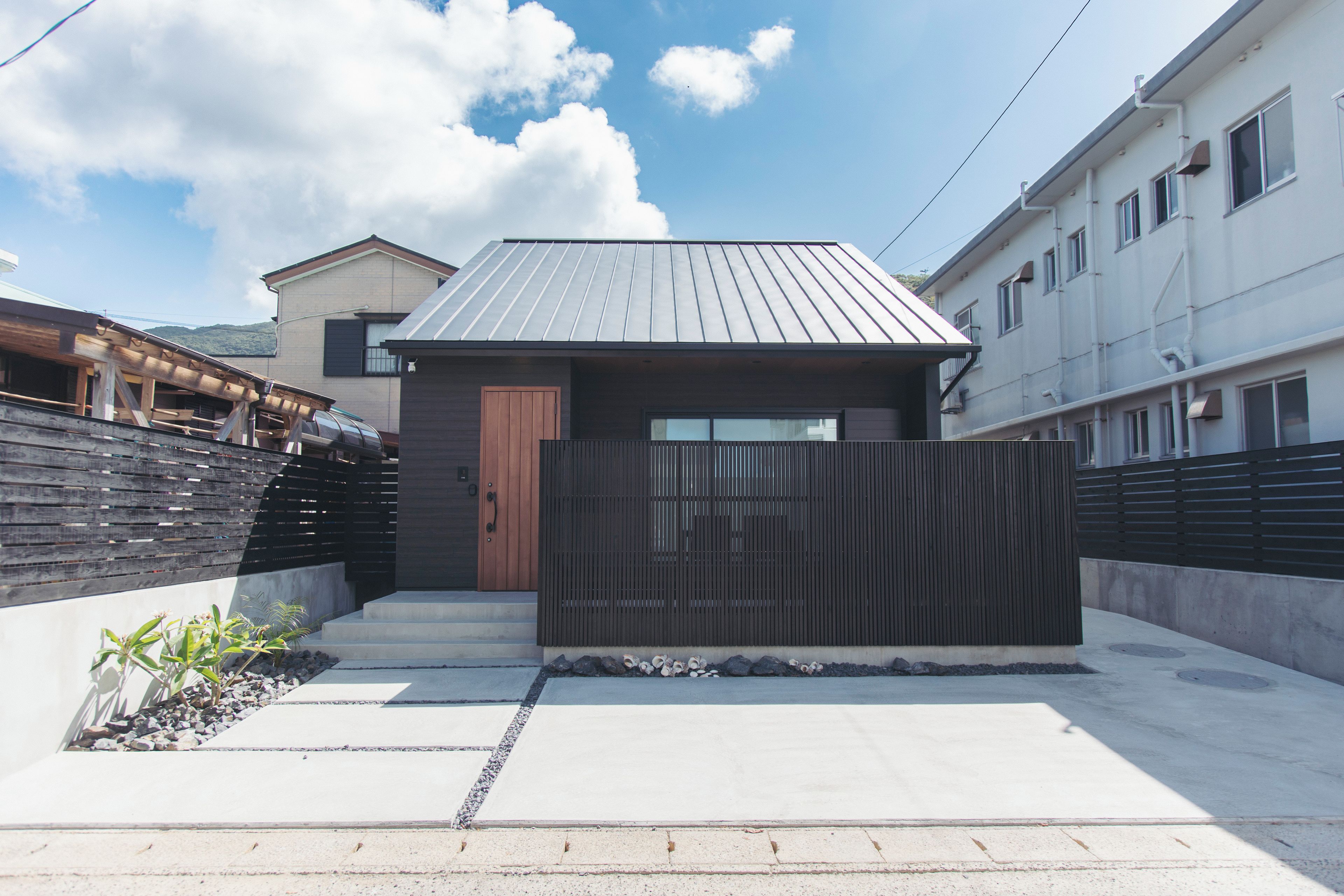 A modern residential building with a metal roof, a wooden door, and a gated entrance.