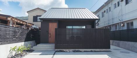 A modern residential building with a metal roof, a wooden door, and a gated entrance.
