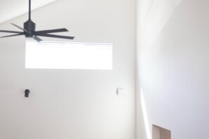 Um ventilador de teto, um interruptor de luz e um termostato em uma parede branca.