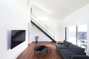 Una sala de estar moderna con una escalera, un televisor de pantalla plana, un sofá gris y una planta en maceta.