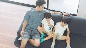 A man and two children sitting on a grey sofa in a room with a large window.