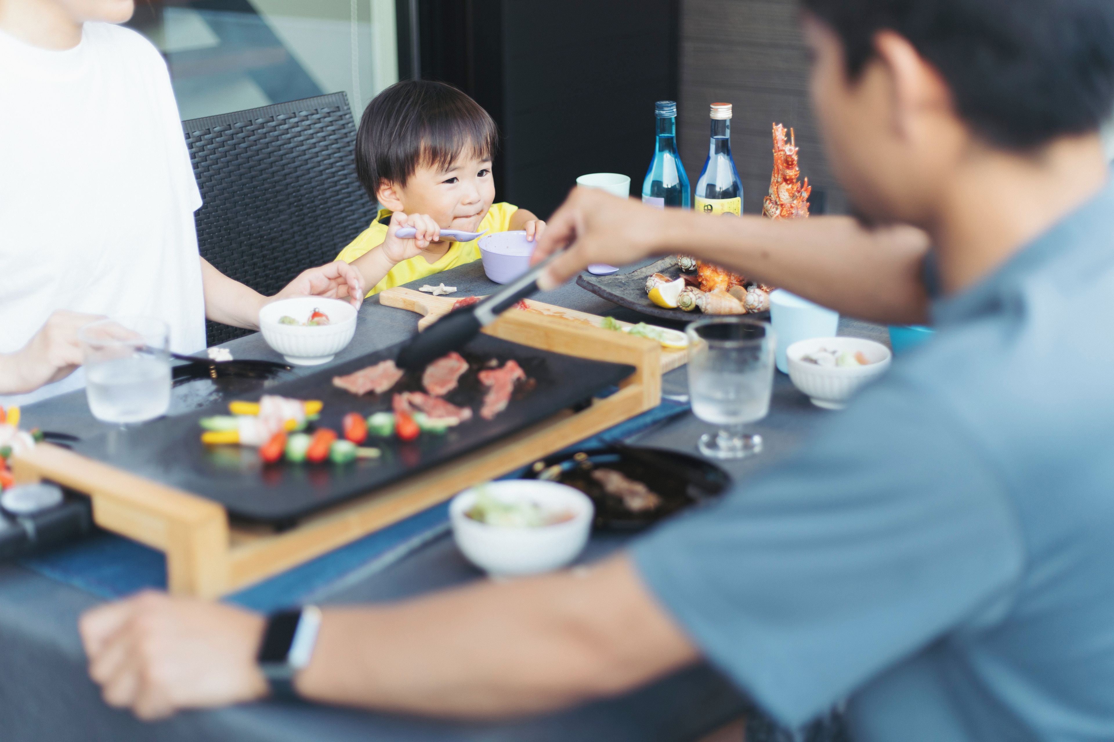 Une table à manger avec de la nourriture, un enfant qui mange et des adultes assis autour.