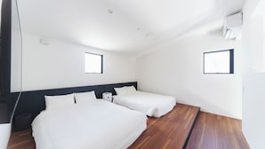 Habitación de hotel con dos camas, piso de madera y una ventana pequeña.