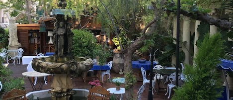 En udendørs terrasse med springvand, siddepladser og plantekasser.