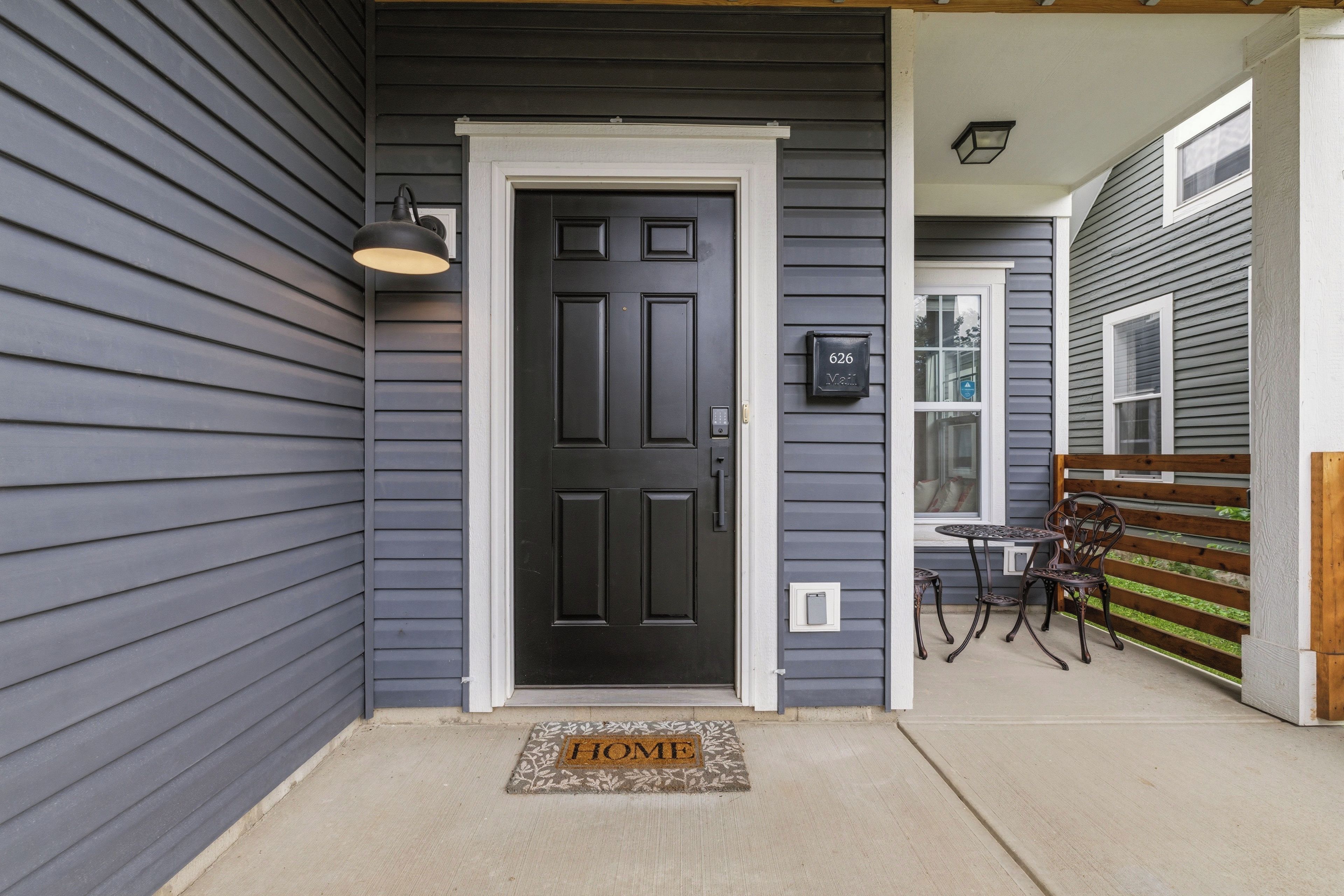A dark gray exterior with a black door, a mailbox, and a small outdoor seating area with a table and chairs.