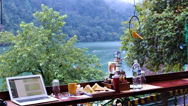 A laptop on a table with a view of a lake and forest. - Treebo Lakeside Inn (Nainital)