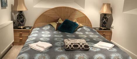 A bedroom with a bed, two bedside tables, two lamps, a radiator, and a window with blinds.