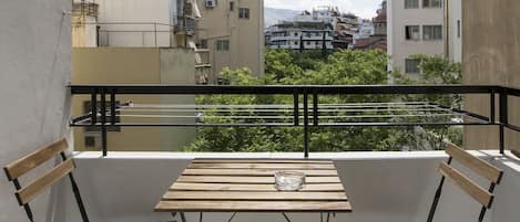 Un balcón con una mesa de madera y dos sillas, con vistas a un paisaje urbano con edificios y zonas verdes.