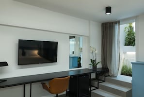 Ett modernt vardagsrum med en platt-TV som är monterad på väggen, en soffa, ett soffbord och en trappa som leder ut till ett utomhusområde.