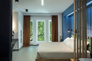 Une chambre moderne avec un grand lit, un bureau et une vue sur les arbres par les fenêtres.