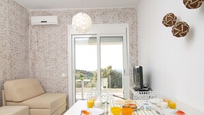 A dining area with a table set for breakfast, a sofa, and a TV on a stand. - Iperion Apartment (Rethymno)