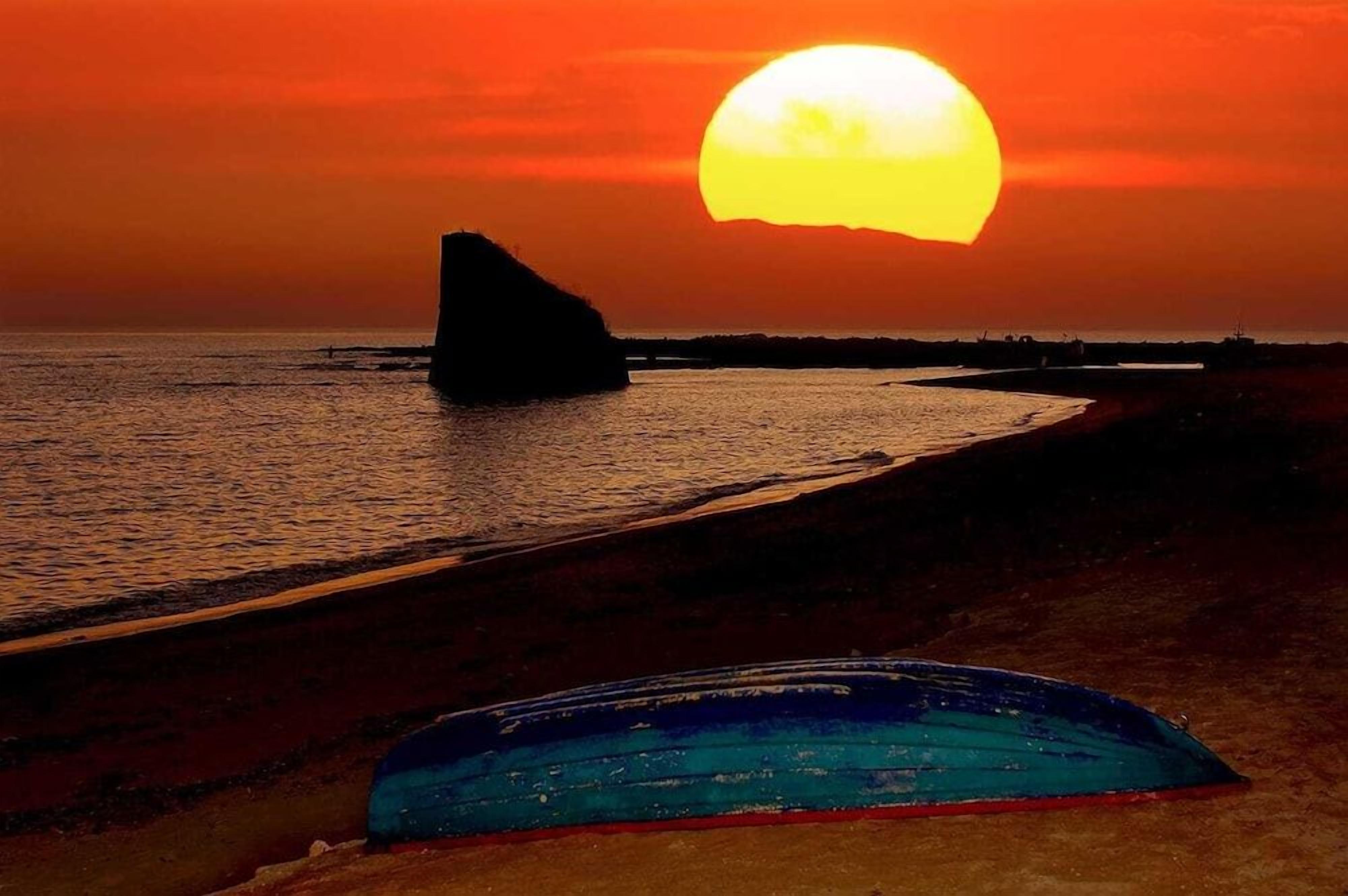 A sunset over a beach with a rock formation and a blue object on the sand.