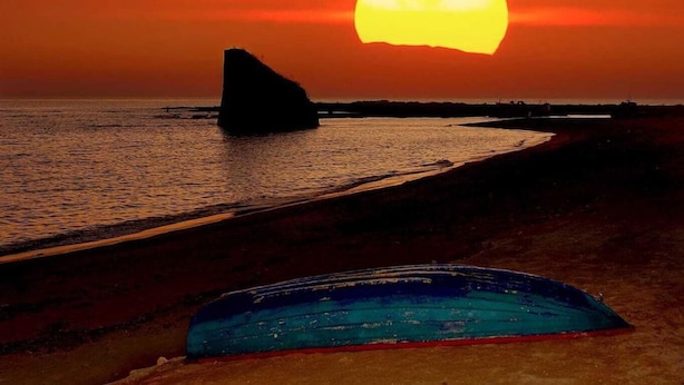 A sunset over a beach with a rock formation and a blue object on the sand. - Bluesky Alloggi (Melendugno)