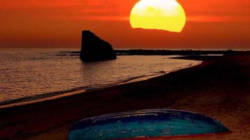 A sunset over a beach with a rock formation and a blue object on the sand.