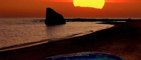 A sunset over a beach with a rock formation and a blue object on the sand.