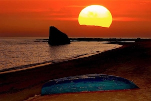 Un atardecer sobre una playa con una formación rocosa y un objeto azul en la arena.