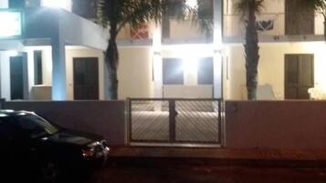 A two-story building with a gated entrance, a parked car, and palm trees.