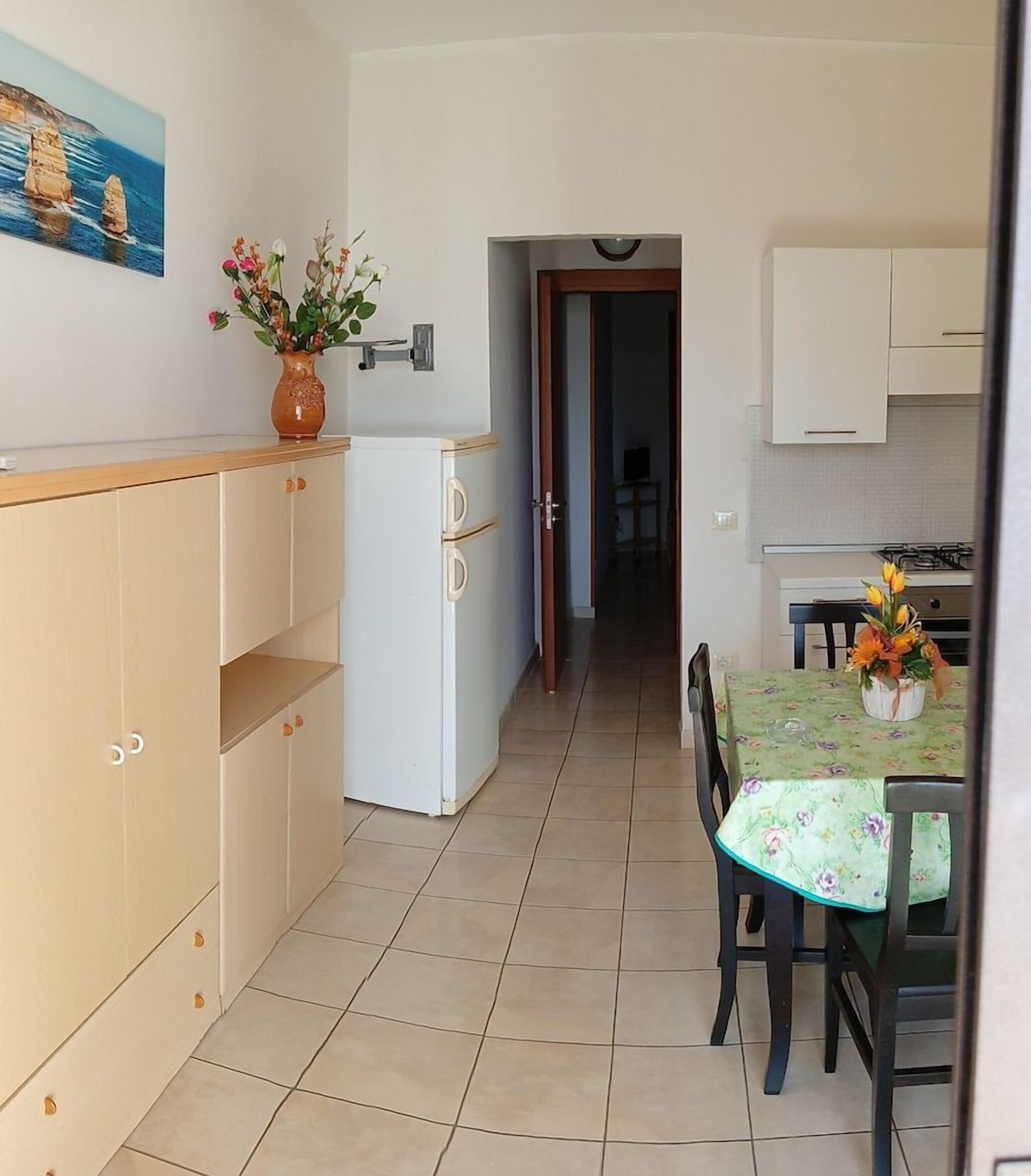 A compact kitchen with a dining area, a white refrigerator, and a vase with flowers on the counter.