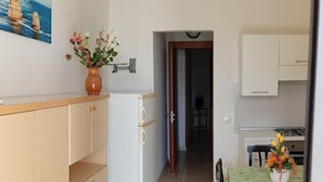 A compact kitchen with a dining area, a white refrigerator, and a vase with flowers on the counter. - Bluesky Alloggi (Melendugno)
