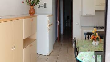 A compact kitchen with a dining area, a white refrigerator, and a vase with flowers on the counter.
