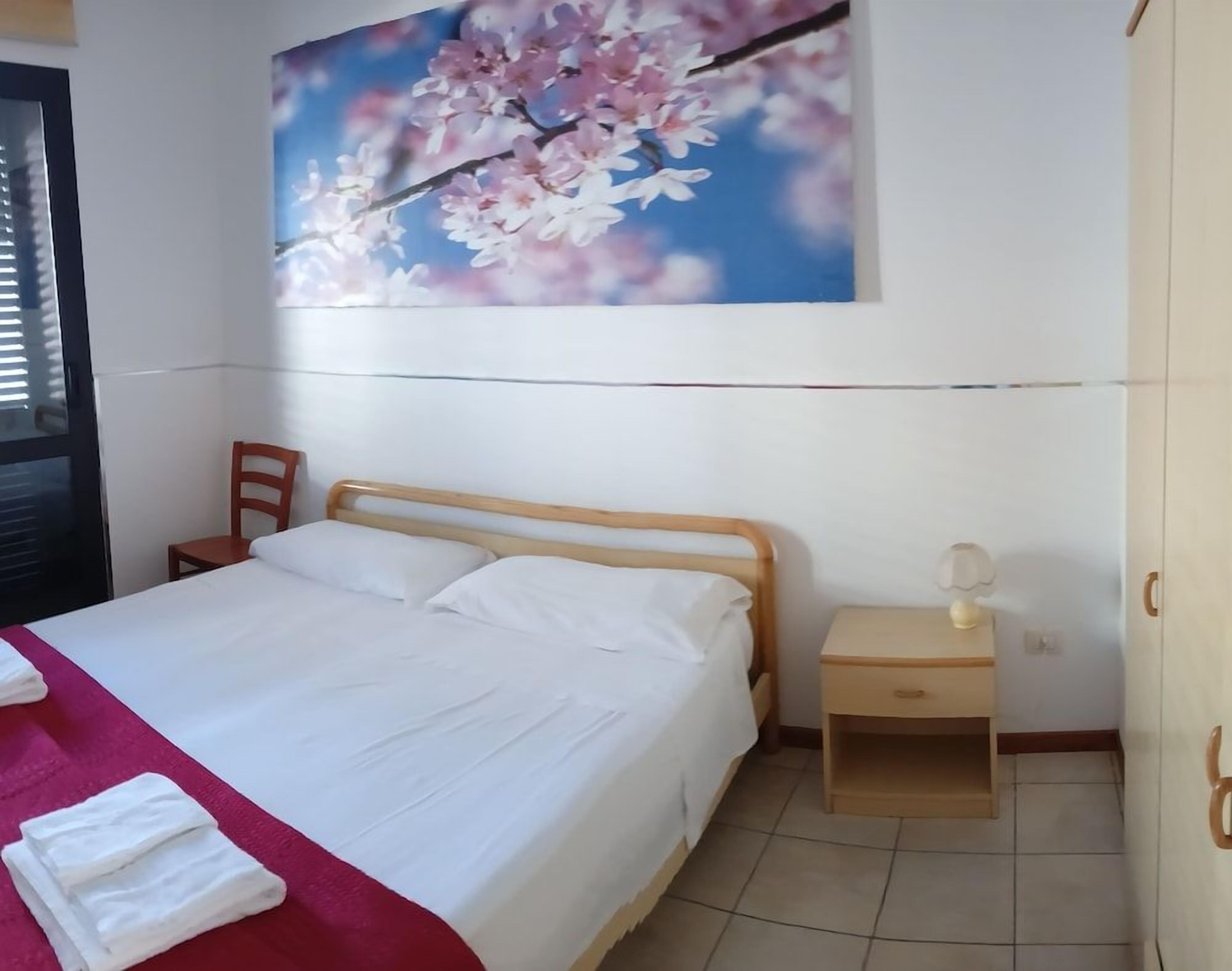 A bedroom with a bed, a nightstand, a chair, a wardrobe, and a wall-mounted painting.