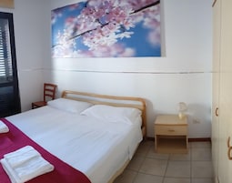 Un dormitorio con cama, mesita de noche, silla, armario y un cuadro colgado en la pared.