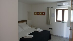 Una camera d'albergo con un letto, un comodino, un condizionatore d'aria, una finestra con tende e un'opera d'arte appesa al muro.