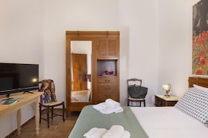 A hotel room with a bed, a television, a desk with a chair, a wardrobe, and a painting on the wall.