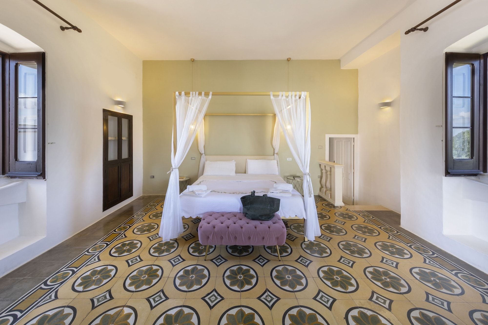 A bedroom with a four-poster bed, a canopy, a tufted bench, and a patterned floor.