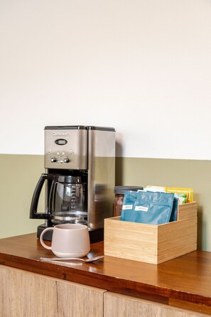 Eine Küchenzeile mit Kaffeemaschine, einer Tasse und einer Holzkiste mit Kaffeekapseln.