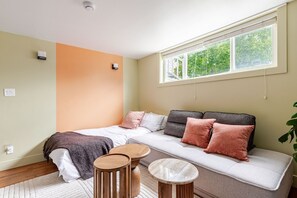Ein modernes Zimmer mit einer Couch, einem Bett, einem kleinen Tisch und einem Fenster mit Blick auf Grünflächen.
