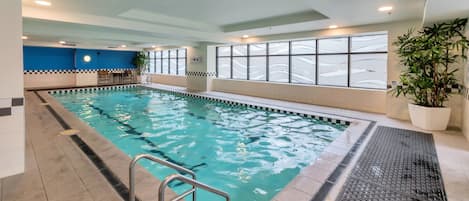 An indoor swimming pool with clear water, a pool ladder, and a potted plant.