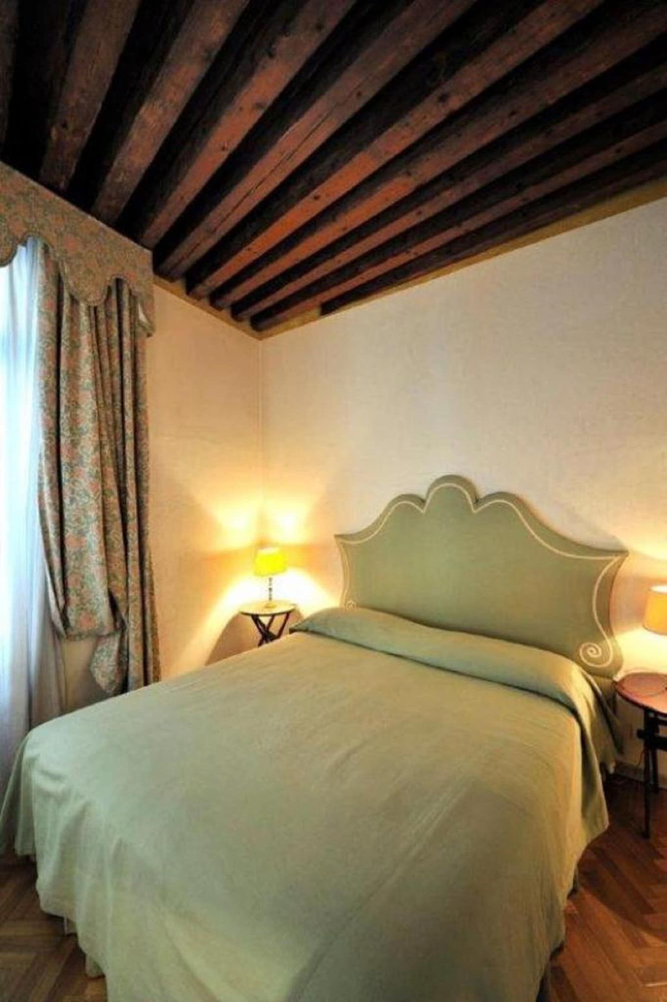 A room with a bed, a nightstand, a lamp, and a window with curtains.