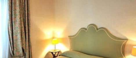 Een kamer met een bed, een nachtkastje, een lamp en een raam met gordijnen.
