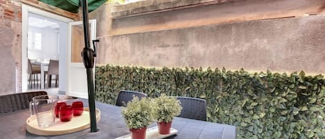 An outdoor patio area with a table, chairs, potted plants, and a green canopy.