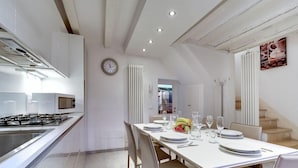 A modern kitchen with a dining area, white cabinetry, a gas stove, and a clock on the wall. - Pozzo Roverso (Venice)