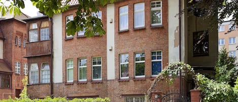 A multi-story brick building with multiple windows, a gated entrance, and surrounding greenery.