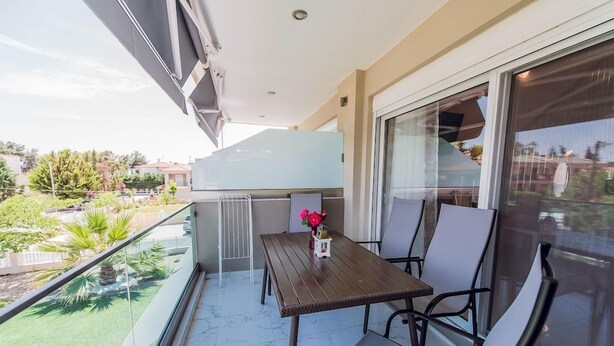 Un balcón con una mesa y sillas, vista a un jardín y un edificio al fondo.