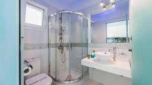 Un baño moderno con ducha envuelta en vidrio, inodoro y lavamanos con espejo arriba.