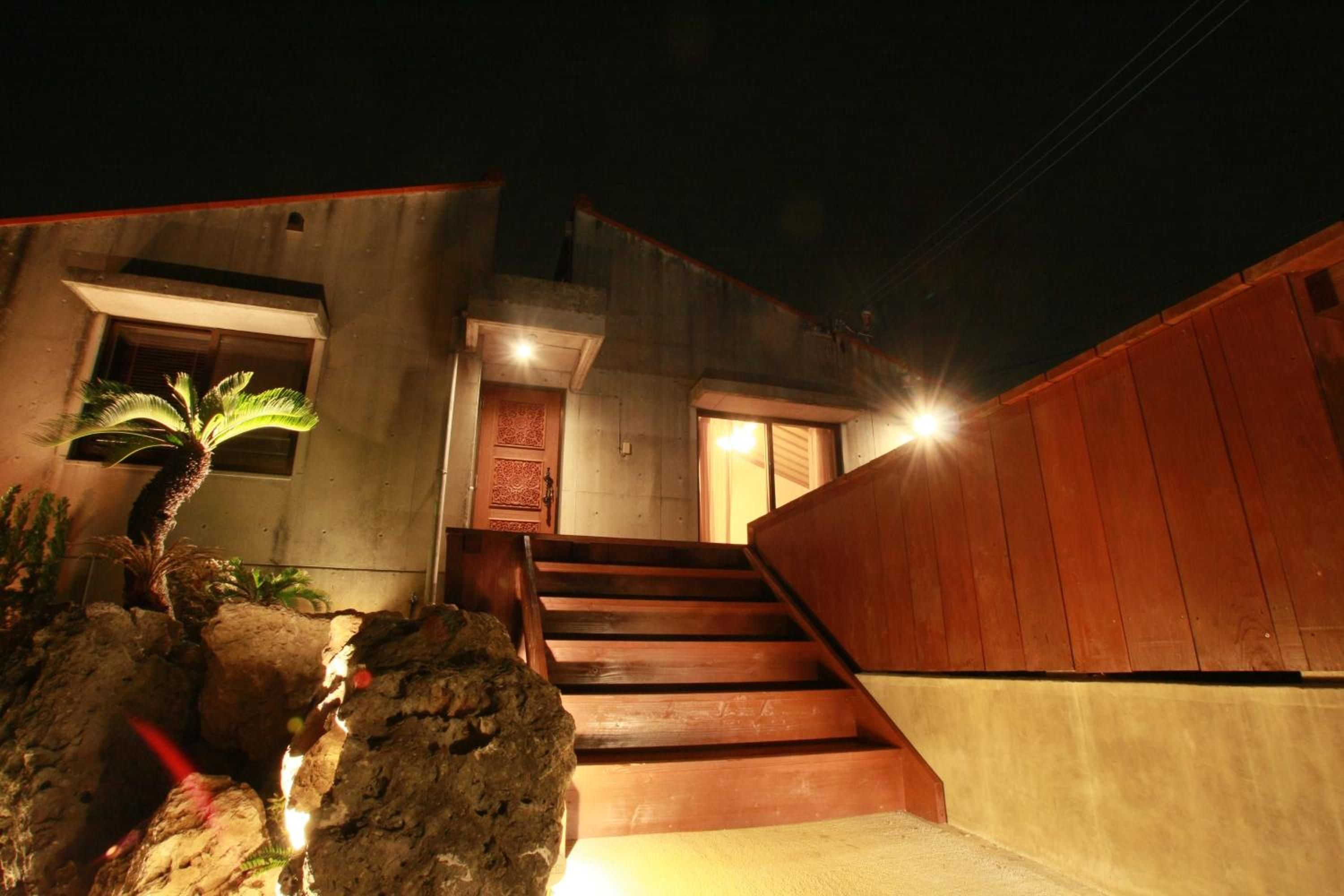 A building with a wooden staircase leading to a door, a small palm tree, and a concrete wall.