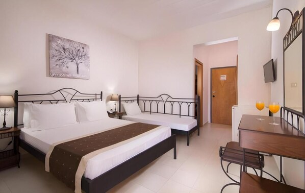 Habitación de hotel con cama doble, mesita de noche con lámpara, pequeño escritorio con silla y televisión en la pared.