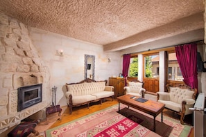 A traditional room with stone walls, a fireplace, and a large window with curtains. - Aja Cappadocia Hotel (Ürgüp)