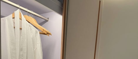 Habitación de hotel con vestidor, cama con ropa de cama blanca, mesita de noche y luz fijada a la pared.