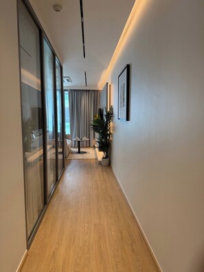 Un pasillo moderno con suelo de madera, una división de vidrio, una planta en maceta y un cuadro en la pared.