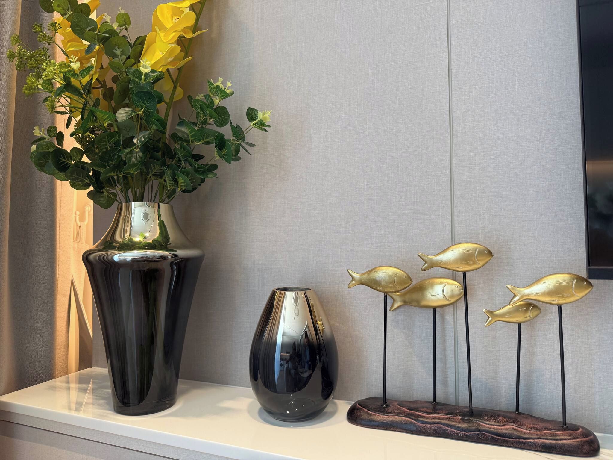 A shelf with a large vase of yellow flowers, a smaller vase, and a decorative fish sculpture.